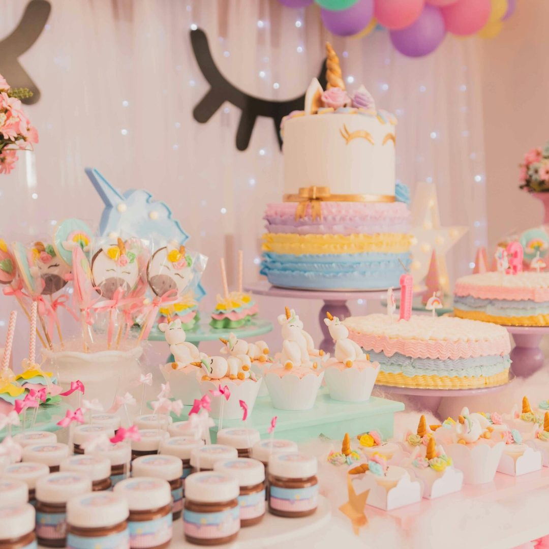 A vibrant unicorn-themed birthday party setup with cakes, cupcakes, and decorations.