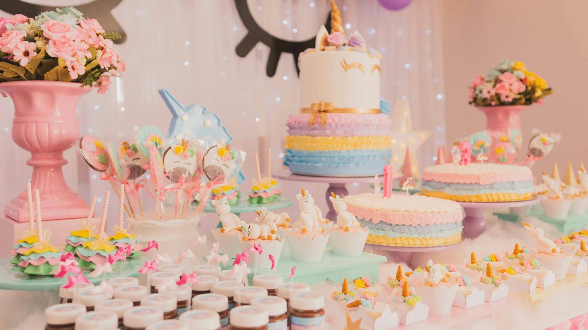 A vibrant unicorn-themed birthday party setup with cakes, cupcakes, and decorations.